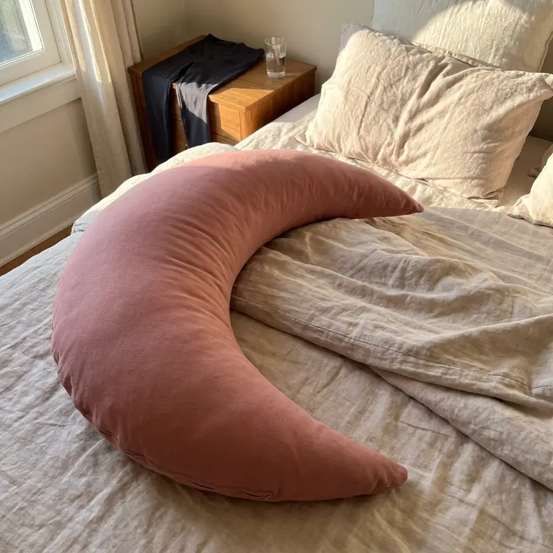 The Cove Pregnancy Pillow in Rosewood on an unmade bed