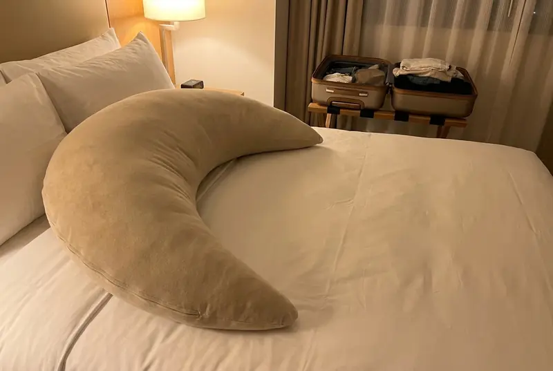An Oat Cove on a white hotel bed beside an open suitcase